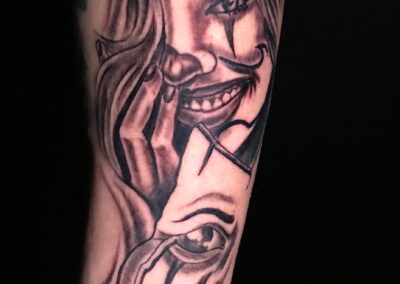 Black and grey realism tattoo featuring a smiling female clown face transforming into a crying theater mask by Clockwork Tattoo Shop in Centereach, Long Island, New York.