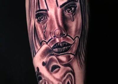 Black and grey realism tattoo of a crying clown woman holding a theatrical mask, by Clockwork Tattoo Shop in Centereach, Long Island, New York.