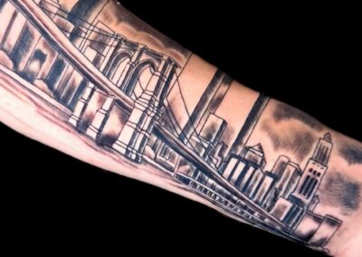 Black and grey realism forearm tattoo featuring the Brooklyn Bridge with the New York City skyline, including detailed architectural linework and smooth shading, professionally tattooed by Clockwork Tattoo Shop in Centereach, Long Island, NY.